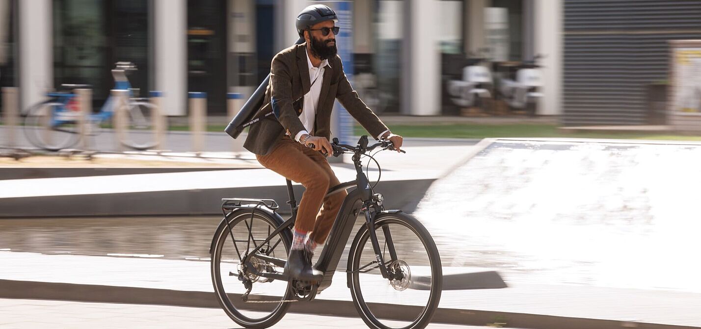 Urbane Mobilität: Geschäftsmann auf einem Elektrofahrrad in der Stadt Ein Pendler fährt auf seinem elektrischen Fahrrad durch das Stadtgebiet.
